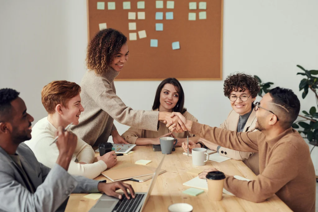 une réunion avec 6 personnes dans un bureau autour d'une table, 2 personnes se serrent la main